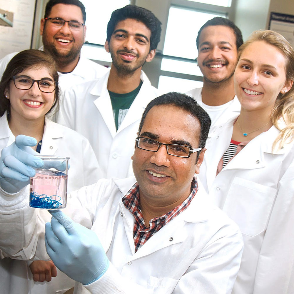 在生物医学实验室，教授举着烧杯，学生们穿着白大褂微笑着