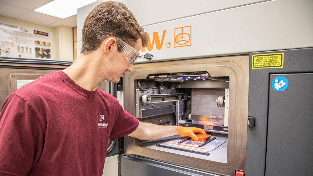 学生放置一个金属物体在一个大型金属添加剂3D打印机。