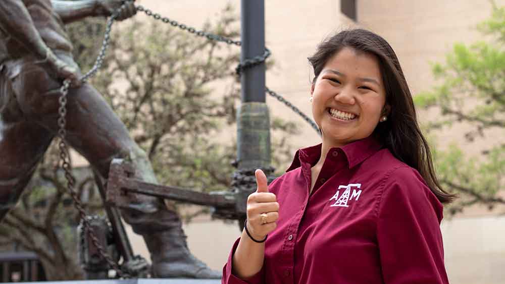 一名石油工程专业的女学生微笑着，做了一个德州农工大学的竖起大拇指的手势